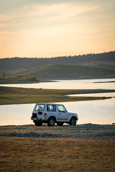 4x4 araba gün batımında Alentejo, Portekiz 'deki güzel kahverengi manzaralı bir gölde.