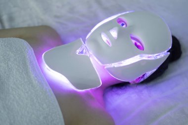 Kozmetik maske. Kız maske takıyor. Promosyon ürünleri. Yüzün sağlığı ve güzelliği. LED Yüz Maskesi, Güzellik Fotonu Terapisi. LED maskeli yenileme tedavisi genç bir kadına uygulanır.