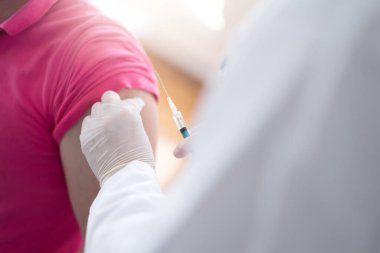 Korunaklı maskeli genç bir kadın doktor Coronavirus ya da ncov 19 'a ya da hastanın koluna aşı enjekte ediyor ya da hazırlıyor.