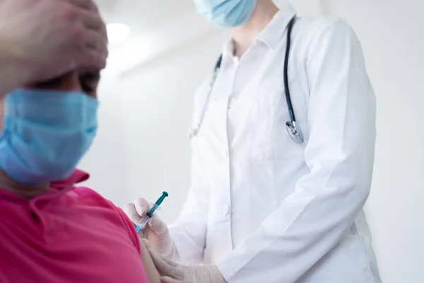 若い女性医師による防護マスクの注射又はコロナウイルスに対するワクチンの注射若しくは準備又は患者の腕に痙攣 — ストック写真