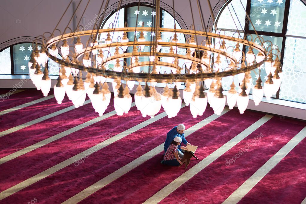 Muslim father and son praying together. Muslim dad and son praying in the mosque and reading holy koran inside the mosque.