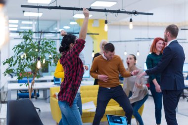 İş kazananlar. Bir grup mutlu genç kutlama yapıyor, el kol hareketi yapıyor, kollarını kaldırıyor ve pozitifliğini ifade ediyor.