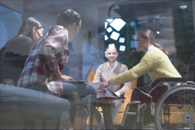 Ofis çalışanları ve tekerlekli sandalyedeki insanlar modern bir ofiste iş konuşuyorlar. Engellilik ve iş konsepti