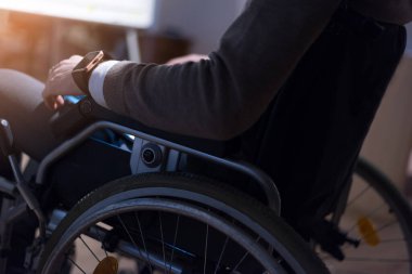 Tekerlekli sandalyedeki genç işadamı, modern işyerinde bilgisayar laptopu kullanıyor.