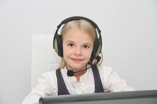 Llittle girl sits in front of a laptop with headphones and learn — Stock Photo, Image