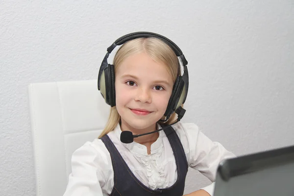 Llittle girl sits in front of a laptop with headphones and learn — Stock Photo, Image