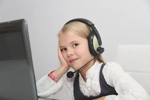 Llittle girl sits in front of a laptop with headphones and learn — Stock Photo, Image