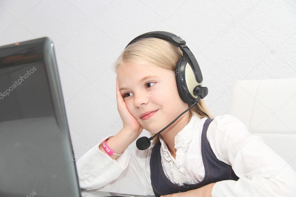 Llittle girl sits in front of a laptop with headphones and learn
