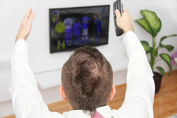 Молодой человек сидит на диване и смотрит футбол по телевизору. — стоковое фото