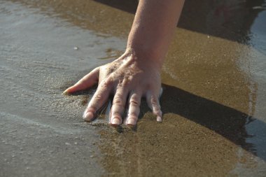 Kadının eli deniz suyuna dokunuyor.