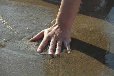 Kadının eli deniz suyuna dokunuyor.