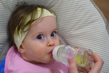 Bebek sandalyesinde otururken biberondan içen şirin bir bebeğin yakın çekimi..