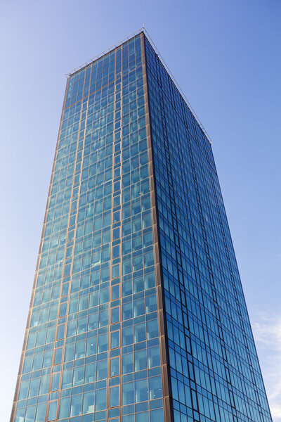 Glass reflective office building skyscraper against blue sky on a sunny day