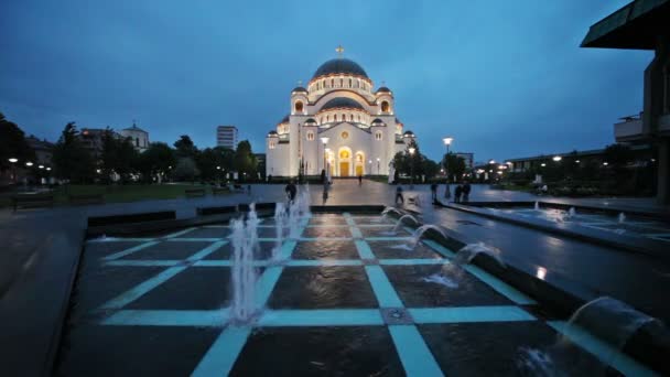 Templo de San Sava en Belgrado, Serbia con fuente en la noche lluviosa con gente que pasa por allí . — Vídeos de Stock