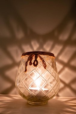 Yanan çay mumuyla kaplı cam mum tutacağı. Yüzeyde yansıması var..