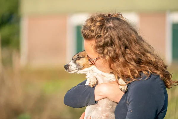 Çiftçi ve onun evcil hayvanlara olan aşkı. Jack Russell Terrier 'in köpeği kadının kollarında yatıyor. arkaplanda sabit.