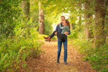 Uzun çocuk sevgilisini sevgiyle ormanda taşıyor. Gülümsüyor, gün ışığında tüm vücudum.