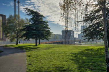 Lahey, 8 Kasım 2020. Lahey, Hollanda 'dan. Şehir merkezinde dumanı tüten boruları olan bir fabrika güneşli bir sonbahar gününde ön planda bisiklet köprüsü. Parktan görüldü. Hollanda 'da..