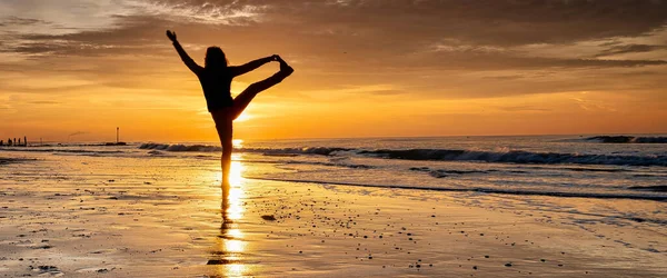 Πανόραμα της γιόγκα στο ηλιοβασίλεμα στην παραλία. Γυναίκα κάνει γιόγκα και απολαμβάνει τη ζωή στη θάλασσα. Μεγάλη κάλυψη ή μέσα κοινωνικής δικτύωσης — Φωτογραφία Αρχείου
