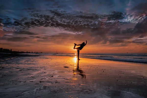 Σιλουέτα μιας νεαρής γυναίκας που κάνει γιόγκα στην παραλία κατά τη διάρκεια ενός όμορφου χρυσαφένιου, μωβ ηλιοβασιλέματος — Φωτογραφία Αρχείου