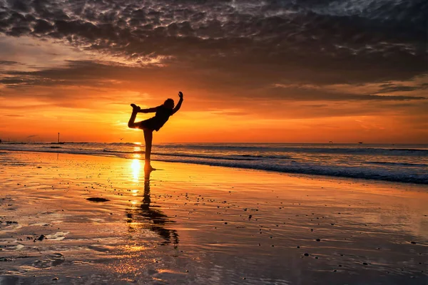 Σιλουέτα μιας γυναίκας που κάνει γιόγκα στην παραλία κατά τη διάρκεια ενός όμορφου ηλιοβασιλέματος — Φωτογραφία Αρχείου