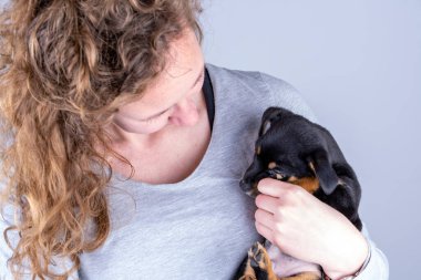 Kahverengi bukleli bir kadın kollarında minik bir Jack Russel Terrier köpeğine sarılıyor.