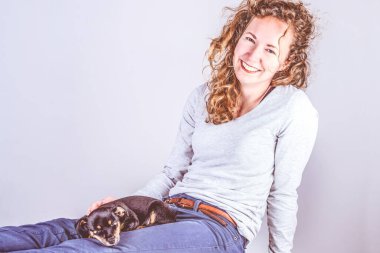 Kıvırcık kahverengi saçlı, bacaklarında Jack Russel Terrier köpeğiyle gülümseyen güzel bir kadının ayrıntıları. Eski, eski renkler