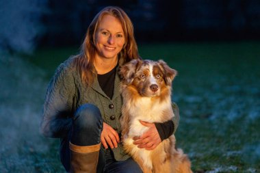 Avustralya çoban köpeği, kamp ateşinin yanında sahibinin yanında oturur. Kadın ve köpek, alacakaranlıkta altın renkli ateşin altında yanarlar. Kışın kamp hayatı