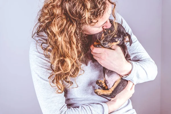 Parte de una mujer con rizos marrones, besa amorosamente a un pequeño cachorro Jack Russel Terrier en sus brazos. en Vintage, colores retro — Foto de Stock