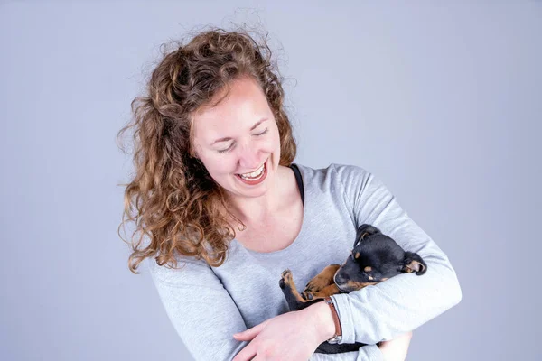 Parte de una mujer sonriente con rizos marrones, sostiene amorosamente a un pequeño cachorro Jack Russel Terrier dormido en sus brazos — Foto de Stock