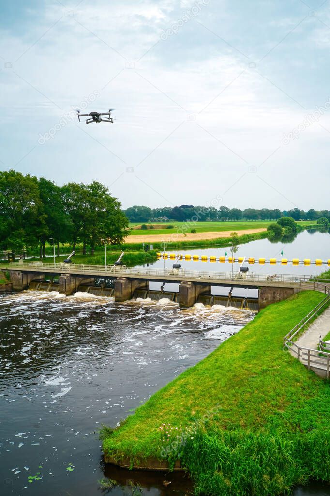 An aerial view with a flying drone in the background above a weir in the river Vecht. Lock keepers house next to the bridge. Fish pass, fish ladder. Overijssel Vecht