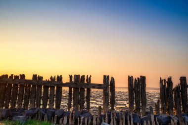 Gün batımında, alçak gelgitte Wadden Denizi manzarası. Renkli dramatik bir gökyüzü. Çamurda siluet olarak tahta direkler. UNESCO. Wadden Deniz Dünyası Mirası.