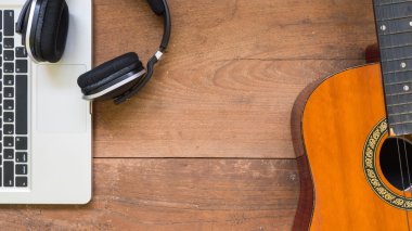Ahşap masa arka plan üzerinde laptop, kulaklık ve akustik gitar ile çalışma alanını üst göster. Metniniz için boş alan.