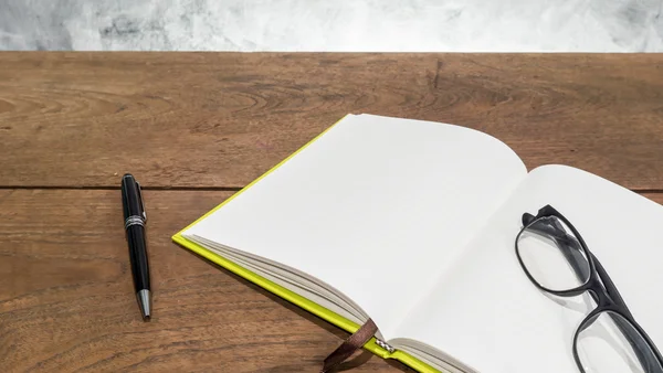 Caderno em branco com caneta e óculos na mesa de madeira . — Fotografia de Stock