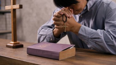 A young Asian Christian man praying to Jesus Christ in a church. clipart