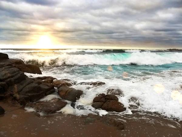 Crashing wave over rocks onto beach — Stock Photo, Image