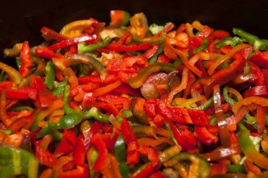 Çok renkli dilimlenmiş biberler dökme demir bir tavada kızartılır. Seçici odak.