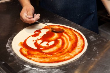Pizza ya da Focaccia yapma süreci. Adım adım talimatlar. Altıncı adım. Aşçı, domates sosunu tabanın her tarafına bulaştırır..
