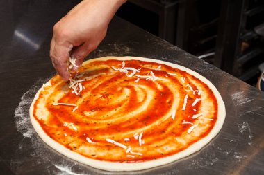 Pizza ya da Focaccia yapma süreci. Adım adım talimatlar. Yedinci adım. Aşçı rendelenmiş peynir ekler.
