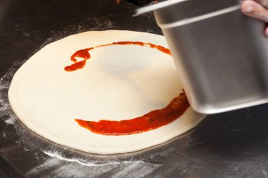 Pizza ya da Focaccia yapma süreci. Adım adım talimatlar. Beşinci adım. Aşçı domates sosunu koymaya başlar..