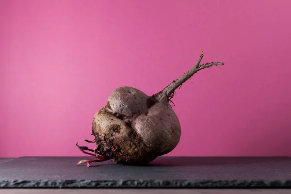Pembe arka planda çirkin pancar kökü, yakın plan. Alışılmadık şekilli sebzeler, organik atıkların azaltılması..