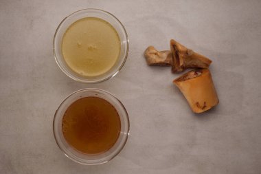 Taş masadaki şeffaf bardaklarda iki çeşit kemik suyu çorbası. Üst taraf, yakın çekim. Balık ve et suyu sağlıklı kolajen içerir..