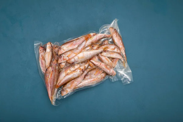 Frozen fish Red mullet (Goatfish) in plastic bag on blue background with copy space. Top view. Mullus barbatus found in Mediterranean Sea, Black Sea and eastern North Atlantic Ocean.