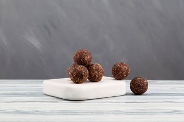 Çiğ vejetaryen tatlılar, enerji topları, fındıklar, kurutulmuş meyveler ve keçiboynuzu tozu. Beyaz tahtada vejetaryen yuvarlak şekerler. Seçici odak, gri arkaplan, boşluğu kopyala.