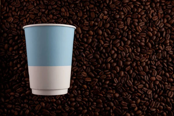 Concept - coffee to take away. Disposable paper cup on the background of roasted coffee beans.