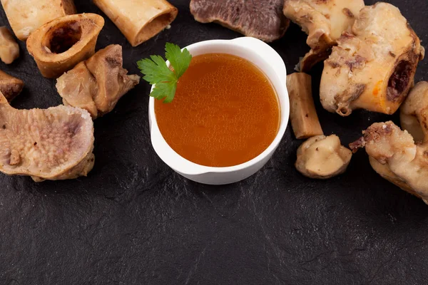 Bone broth on a stone surface next to boiled beef bones. Selective focus, copy space.