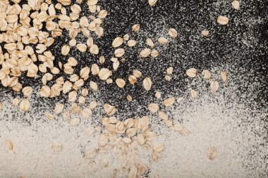 Yulaf gevreği ve yulaf unu karanlık yüzeye saçılmış. Tasarım ögesi, yemek arkaplanı, üst görünüm.