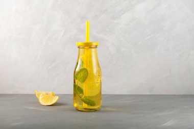 Limon, bal ve naneli yaz içeceği. Gri arka planda sarı şeffaf cam şişe. Metnin için boşluk.