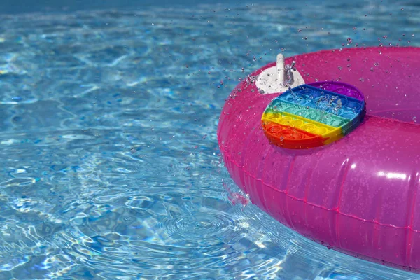 Trendy Pop it Fidget toy and fragment Inflatable ring in swimming pool. Summer day. Splash of water.