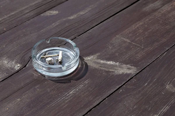 Ashtray with cigarette butts on wooden table. Concept against passive smoking that leads to lung cancer and other diseases.